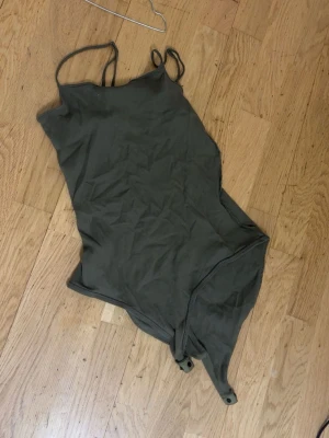 Olivgrön body med smala axelband - Snygg olivgrön body med smala axelband och tryckknappar i grenen. Enkel och stilren design, perfekt att matcha med jeans eller kjol. Tillverkad i mjukt stretchigt tyg för skön passform.