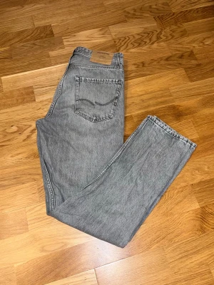 Grå jeans från Jack & Jones - Snygga grå jeans från Jack & Jones med klassisk femficksdesign och raka ben. Jeansen har en ljusgrå tvätt och en patch med logga bak i midjan. Perfekta till en avslappnad stil och passar till det mesta.