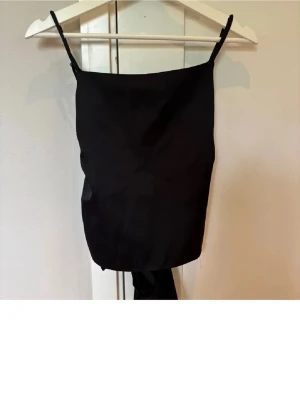 Svart knyttopp från Zara - Snygg svart linnetopp med tunna axelband och knytband i ryggen i satin material. Toppen är i nytt skick då den aldrig kommit till användning 