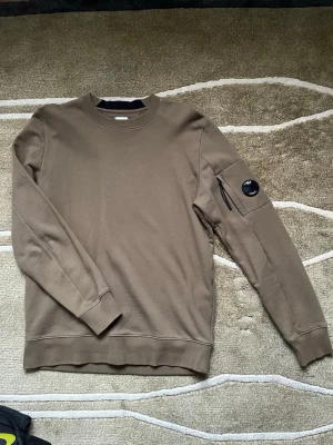 Mörkgrön sweatshirt från C.P. Company - Säljer en fet mörkgrön (ser ut som brun på bilden) sweatshirt från C.P. Company som tyvärr inte kommer till användning. Tröjan är nästan i nyskick, inga tecken på användning alls och är givetvis äkta. Storleken är passar M-L. Skriv gärna vid funderingar 😁