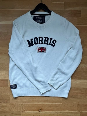 Morris Stockholm stickad tröja – vit färg – Storlek Medium - Klassisk stickad tröja från Morris Stockholm i en snygg vit färg. Ikoniskt broderi med logga och flagga på bröstet. • Storlek: Medium (M) • Färg: vit • Skick: fint skick, som på bilderna ☺️ • Detaljer: Ribbstickade muddar och logotyp-patch nedtill. Hör av dig vid frågor 🤗☺️
