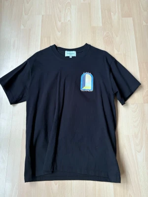 Svart Casa Blanca t-shirt med tryck - Snygg svart t-shirt från Casa Blanca med färgglatt grafiskt tryck i blått, gult och vitt både fram och bak. Klassisk passform och rund halsringning. Tillverkad i mjuk bomull som känns skön mot huden. Perfekt för dig som gillar streetwear och unika prints.
