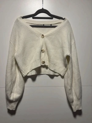 Vit cropped kofta med knappar - Säljer en vit cropped kofta från shein med tre stora knappar framtill. Koftan har v-ringning, ribbstickade muddar och är gjord i ett mjukt stickat material. Perfekt för lager på lager och ger en chill vibe till outfiten.