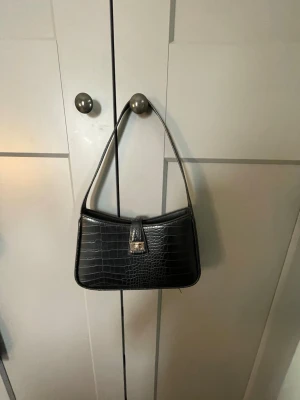 Jätte fin svart handväska med guld detaljer💕 - Nu säljer jag min jätte fina handväska för den inte kommer till användning från hm som är kanske 1 år gammal men har inte använder mycekt så är i fint skick. Har ett fack med dragkedja i väskan💕