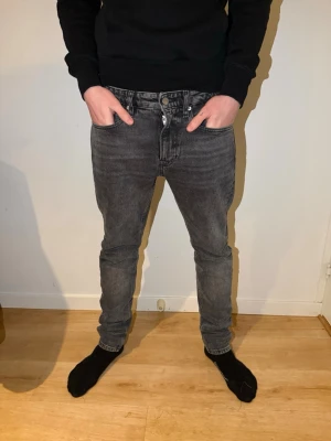 Grå slim fit jeans - Säljer ett par grå slim fit jeans med klassisk femficksmodell och knappgylf. Jeansen har en tvättad look och smal passform som sitter snyggt längs benen. Perfekta för en avslappnad och trendig stil.