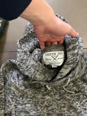 Gråmelerad hoodie från Denim Day - Säljer en gråmelerad hoodie från Denim Day med stor huva och dragsko. Hoodien har en klassisk känguruficka framtill och ribbade muddar vid ärmslut och nederkant. Perfekt för en avslappnad och stilren look.