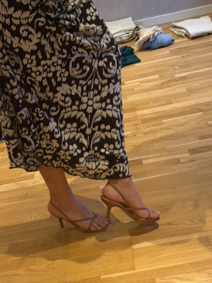 Bruna strappy sandaler med klack - Säljer ett par stilrena bruna sandaler med smala remmar och öppen tå. Sandalerna har en elegant klack och minimalistisk design som passar perfekt till sommarens outfits. Materialet ser konstläder. Supersnygga till både klänning och jeans speciellt till sommaren. Passar till exakt allt