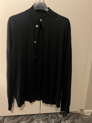 Marinblå klassisk kofta med knappar - En stilren marinblå kofta med långa ärmar och knäppning framtill. Koftan har ribbade muddar vid ärmslut och nederkant samt en högre krage. Perfekt att slänga över en t-shirt eller skjorta för en clean look.