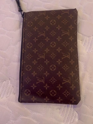  monogram plånbok - Snygg brun plånbok med klassiskt monogrammönster och dragkedja upptill. Tillverkad i tåligt canvasmaterial med loggor och blommor över hela ytan. Perfekt för kort, cash och småprylar.
