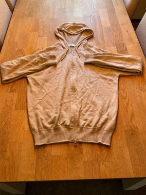 Beige cashmere hoodie från Gran Sasso - Snygg beige hoodie från Gran Sasso i mjuk cashmere. Hoodien har dragkedja framtill, dragsko i huvan och ribbade muddar vid ärmslut och nederkant. Perfekt för dig som gillar stilrena och bekväma plagg med exklusiv känsla. Otroligt mjuk och skön hoodie