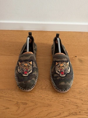 Kamouflage espadrillos - Säljer ett par loafers från Polo i kamouflagemönstrad canvas med ikonisk tigerbrodyr framtill. Mycket sköna nu under sommaren och är oerhört snygga. Hör av er vid minsta fundering!