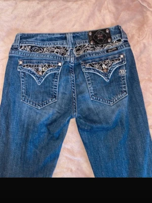 Blå Miss Me jeans med brodyr - Säljer ett par blå jeans från Miss Me med snygga broderade detaljer och nitar på bakfickorna. Jeansen har bootcut-modell och coola kontrastsömmar. Storlek 31 men passar 29-31 enligt mig!💕 skriv gärna vid frågor!