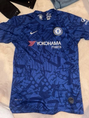 Chelsea FC matchtröja blå - Chelsea FC matchtröja i blått med grafiskt mönster, officiell klubbmärke och sponsortryck. Dri-FIT-material för bra ventilation. Nummer 7 och KANTE på ryggen. Perfekt för fotbollsfans som vill bära sitt favoritlag.
