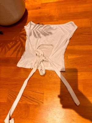 Vit omlottopp från Gina Tricot - Säljer en vit omlottopp från Gina Tricot i mjuk bomull. Toppen har korta ärmar och långa knytband i midjan som ger en snygg och justerbar passform. Perfekt till jeans eller kjol för en fräsch look.