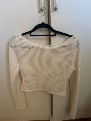 Vit stickad croppad tröja - Säljer en vit stickad croppad tröja med lång ärm och bred, rund halsringning. Tröjan har ett luftigt och grovt stickat mönster som ger en avslappnad och trendig look. Perfekt att styla med höga jeans eller kjol.