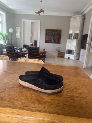 Birkenstock Naples - Säljer ett par svarta tofflor i mocka med bred rem och platåsula i kork. Yttersulan är i gummi för extra grepp. Tofflorna har en stilren och modern look, perfekta för dig som gillar en avslappnad men trendig stil. Nästan helt nya, har använt dom väldigt få gånger. Jätte fina med shorts och linne byxor perfekt till sommaren.