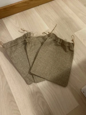 Tre små jutesäckar med snörning - Säljer tre stycken små påsar i naturfärgad jute med snörning upptill. Perfekta för förvaring av småsaker eller presenter. Påsarna har en enkel, rustik look och är ca 20 cm höga. 