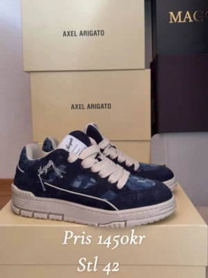 Axel Arigato blå sneakers stl 42 - Snygga sneakers från Axel Arigato i mörkblå mocka och denim med vita detaljer och breda vita skosnören. Skorna har en chunky vit sula och broderad logga på sidan. Perfekta för dig som vill ha en unik och trendig look.