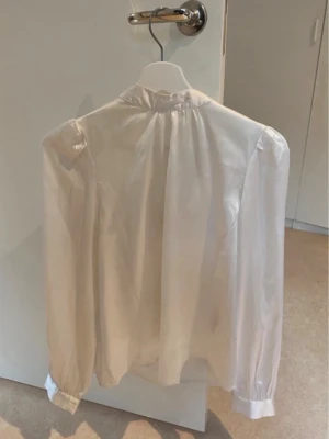 Vit transparent blus med lång ärm - Stilren vit blus i transparent material med lång ärm och lätt puff vid axlarna. Blusen har klassisk krage och knäppning vid ärmsluten, perfekt för en chic och trendig look. Använd fåtal gånger
