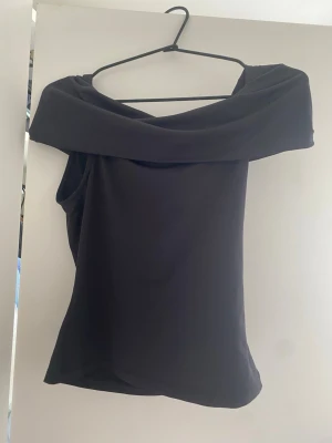Svart offshoulder topp - Stilren svart offshoulder topp med bred krage som vilar över axlarna. Tunn och mjuk känsla i materialet, perfekt för dig som gillar minimalistisk och trendig stil. Snygg att matcha med både jeans och kjol.