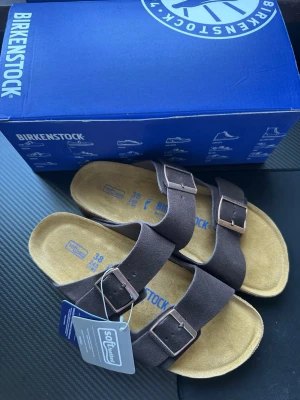 Bruna Birkenstock Arizona sandaler - Säljer helt nya par bruna Birkenstock Arizona sandaler i mocka med två breda remmar och justerbara metallspännen. Fotbädden är mjuk och innersulan är beige. Klassisk och bekväm modell som passar perfekt till sommaren.