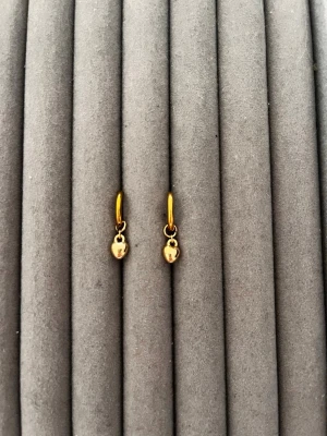 Guldiga örhängen med små berlocker - Snygga örhängen i guldfärgad metall med små runda berlocker som hänger ned. Enkla hoops med minimalistisk design, perfekta för att ge en stilren touch till din look. Passar dig som gillar diskreta men trendiga accessoarer.