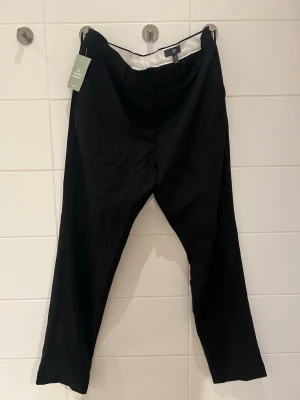 Svarta kostymbyxor från H&M - Snygga svarta kostymbyxor från H&M med klassisk rak passform och diskreta fickor bak. Byxorna har bälteshällor och är tillverkade i ett tunt, mjukt tyg som ger en clean look. Perfekta för dig som vill ha en stilren och enkel outfit.