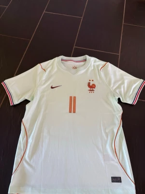 Frankrike fotbollströja Nike Olise - Perfekt Frankrike tröja nu när Frankrike är klara för slutspel i VM! Snygg ljus fotbollströja från Nike med Frankrikes landslagsemblem och nummer 11 på bröstet. Röd Nike-logga och detaljer i rött och blått på ärmsluten. På ryggen står det OLlSE och nummer 11 i rött. Perfekt för match eller träning. Kom med prisförslag och har ni några frågor är det bara att ställa!