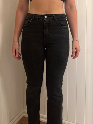 Svarta raka jeans med hög midja - Säljer ett par svarta jeans med hög midja och raka ben. Jeansen har klassisk femficksdesign och knappgylf. Materialet är denim med en lätt tvättad look som ger en avslappnad vibe. Perfekta till både sneakers och boots.