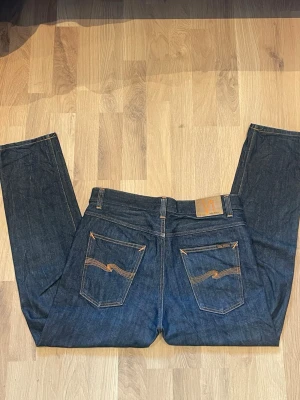 Nudie Steady Eddie II Selvedge - Säljer ett par Nudie Jeans Steady Eddie II Dry Gene i storlek W34/L30.  Jeansen är i mycket fint skick och har väldigt lite användning. Mörk rådenim (dry denim) med i princip inga fades, vilket gör att nästa ägare kan nöta in dem själv och få personliga slitningar.  * Modell: Steady Eddie II * Tvätt: Dry Gene * Storlek: W34/L30 * 100 % bomull * Mycket fint skick * Inga hål eller skador * Selvedge Skicka gärna meddelande vid frågor eller om du vill ha fler bilder.  Priset är inte hugget i sten👍