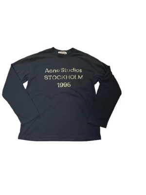 Acne Studios blå longsleeve  - Snygg blå långärmad topp från Acne Studios med tryck i vitt framtill: 'Acne Studios STOCKHOLM 1996'. Tillverkad i mjuk bomull och har en klassisk, normal passform. Perfekt för en clean och stilren look.