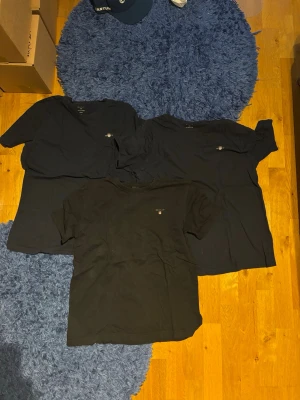 Svarta t-shirts från Gant 3-pack - Säljer tre klassiska svarta t-shirts från Gant med liten broderad logga på bröstet. T-shirtsen har rund hals och korta ärmar, perfekta till jeans eller shorts. Tillverkade i mjuk bomull för skön känsla hela dagen. 2 mörkblåa och en svart den svarta och den ena mörkblåa är 170. Den andra mörkblåa är 176 cm i storlek.