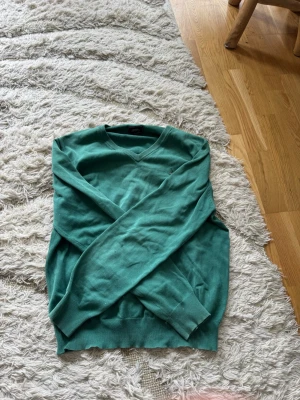 Grön stickad tröja från Boomerang - Snygg grön stickad tröja från Boomerang med V-ringning och ribbade muddar. Perfekt för lager-på-lager och enkel att matcha med jeans eller kjol. Klassisk modell med mjukt material som känns skönt mot huden.