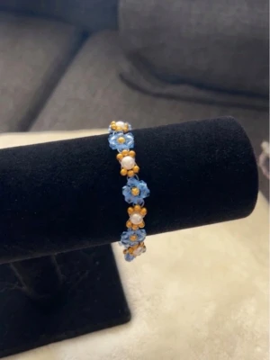 Blått pärlarmband med blommor -  armband med små blå blommor av pärlor, varvat med vita och guldfärgade pärlor. 