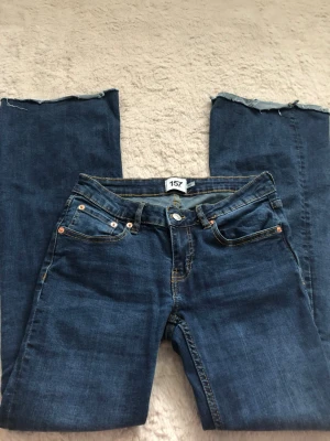 Mörkblå raka jeans från 157 - Säljer ett par mörkblå jeans från 157 med raka ben och råa, avklippta benslut för en trendig look. Klassisk femficksmodell med kontrastsömmar och knappgylf. Perfekta för dig som gillar en avslappnad och cool stil.