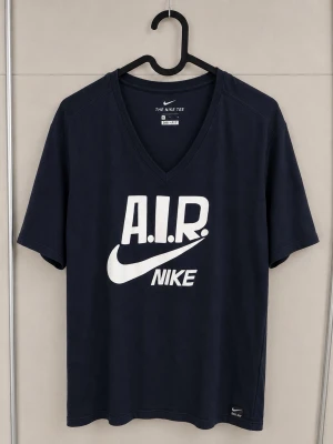 Mörkblå Nike AIR t-shirt v-ringad - Snygg mörkblå t-shirt från Nike med stor vit AIR-logga och swoosh på bröstet. T-shirten har v-ringning och korta ärmar. Tillverkad i Dri-FIT-material som andas, perfekt för en aktiv livsstil. Storlek M, men går även bra som S.