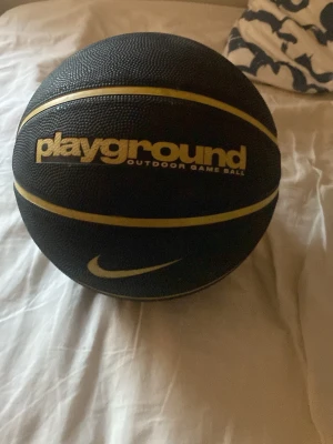Nike Playground svart basketboll - Basketboll från Nike i svart med gula linjer och texten 'playground outdoor game ball'. Bollen är rund och tillverkad i tåligt gummi, perfekt för utomhusspel och streetbasket. Snygg design med tydlig Nike-logga.