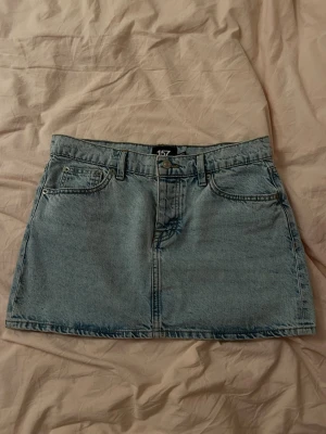 Ljusblå jeanskjol från 157 - Trendig ljusblå jeanskjol från 157 med klassisk femficksdesign och knappstängning fram. Kjolen har bälteshällor och är i en kort modell, perfekt till vardagslooken. Tillverkad i slitstarkt denimtyg.