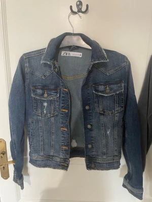 Blå jeansjacka från Zara XS - Snygg blå jeansjacka från Zara i storlek XS. Klassisk modell med två bröstfickor med lock och knappar, slitna detaljer och kontrastsömmar. Perfekt till lager på lager och ger en cool vibe till din outfit.