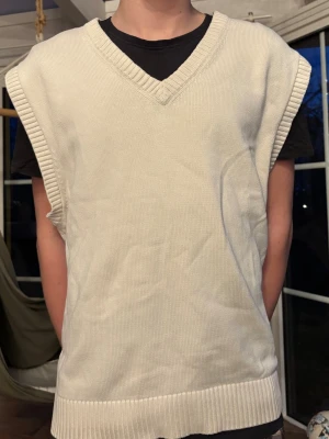 Beige stickad väst med v-ringning - Snygg beige stickad väst med bred ribbad v-ringning och ribbade kanter. Perfekt att slänga över en t-shirt eller skjorta för en clean och stilren look. Västen har en loose passform och är riktigt skön att bära.