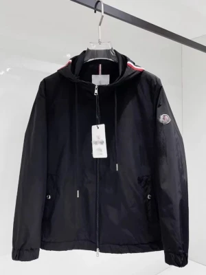 Moncler vindjacka Windbreaker - Snygg svart vindjacka från Moncler med huva och dragkedja framtill. Jackan har två fickor med tryckknappar, justerbar dragsko i midjan och Moncler-logga på ärmen. Detaljer i rött och vitt vid huvan ger en sportig touch. Tillverkad i lätt, vindtätt material.