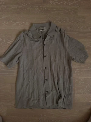 Beige kortärmad skjorta från COS - Stilren beige skjorta från COS med korta ärmar och knappar framtill. Skjortan har en klassisk krage och är tillverkad i ett mjukt material med diskret struktur. Perfekt för en avslappnad men snygg look.