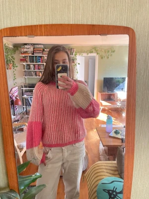 Randig stickad tröja i rosa och beige - En cool stickad tröja med breda ränder i rosa och beige. Tröjan har ballongärmar med färgblock och ribbstickad hals, ärmslut och nederkant. Perfekt för dig som gillar färg och oversized look. Materialet ser ut att vara mjukt och ulligt.