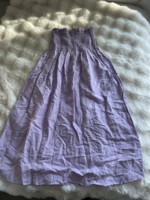 Ljuslila långkjol från Kappahl - Supersöt ljuslila långkjol från Kappahl med smock i midjan och volangdetalj upptill. Kjolen är i ett mjukt och lätt bomullstyg, perfekt för varma dagar. Den har en avslappnad passform och faller snyggt längs benen. Använd ett fåtal gånger och är som ny. 