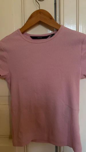 Ljusrosa ribbad topp från Vero Moda - Säljer en ljusrosa ribbad topp från Vero Moda. Modellen är croppad med korta ärmar och har en slim passform som framhäver siluetten. Materialet är mjukt och stretchigt, perfekt för dig som gillar en enkel och clean look. Tröjan är oanvänd men utan prislapp/förpackning. 