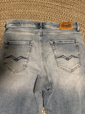 Ljusblå jeans från Replay - Snygga ljusblå jeans från Replay med klassisk femficksmodell och diskreta slitningar. Bakfickorna har ett coolt broderat mönster och jeansen har en patch med Replay-logga bak i midjan. Modellen heter Thad och materialet är bomull med stretch. W 28 L 32