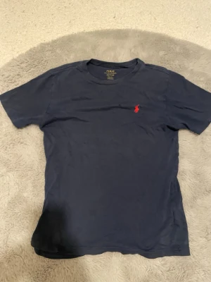 Mörkblå t-shirt från Polo Ralph Lauren - Mörkblå t-shirt från Polo Ralph Lauren med klassisk röd broderad logga på bröstet. Låga priset pga 2 små hål på den (se på bild)