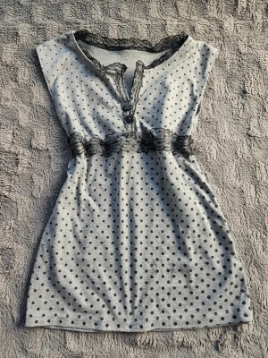 Grått nattlinne med spets och prickar - Sött topp med svarta prickar och dekorativ svart spets vid halsringning och midja. Knappar framtill och ärmlös design som ger en avslappnad och bekväm känsla. Handgjord och har därav ingen lapp