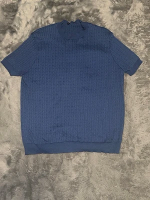 Marinblå stickad topp med kort ärm - En marinblå stickad topp med korta ärmar och diskret strukturmönster. Toppen har rund halsringning och ribbade kanter vid ärmslut och nederkant. Perfekt för dig som gillar en enkel men ändå stilren look.