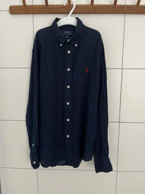 Mörkblå skjorta från Polo Ralph Lauren - Säljer nu min mörkblå Ralph Lauren linne skjorta som blivit förliten. Dem är i ett mycket bra skick. Den har ett rött Ralp Lauren märke och är i storlek 10/12 år. Vid andra frågor eller funderingar så är det bara att höra av sig.